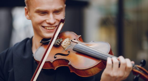 A young beautiful redhead boy playing the violin in a summer city