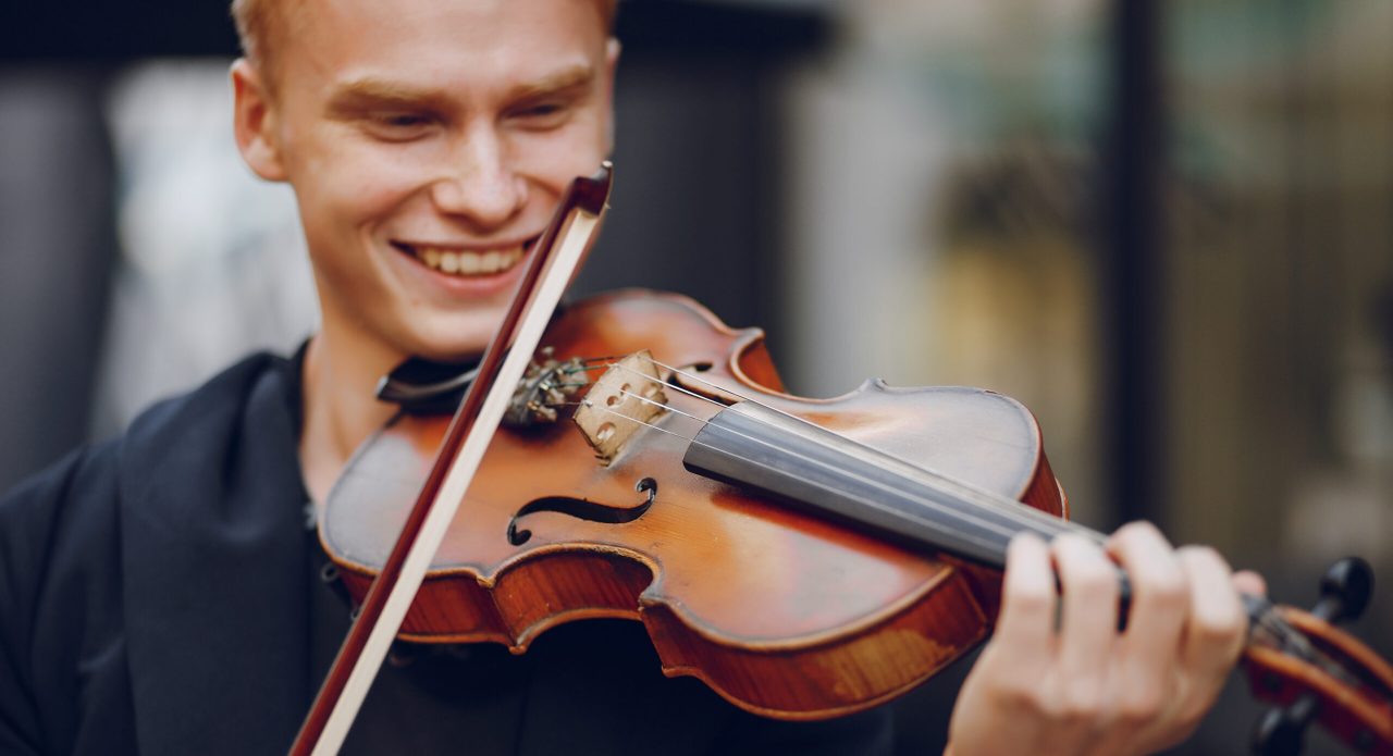 A young beautiful redhead boy playing the violin in a summer city